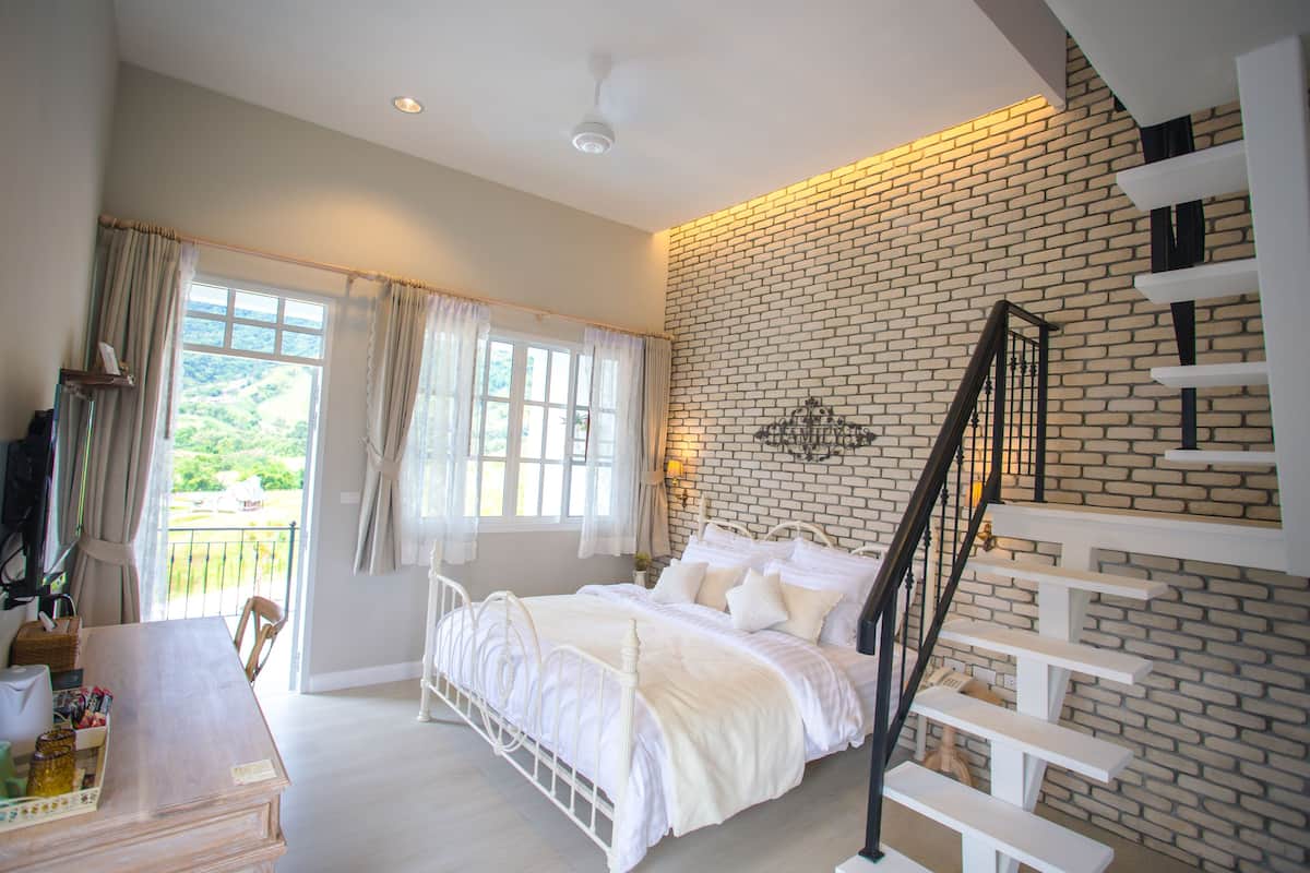 Une chambre avec un lit blanc, un mur en briques et un escalier.