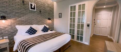A bedroom with a brick wall, a bed with white bedding, a ceiling fan, and a wooden floor.