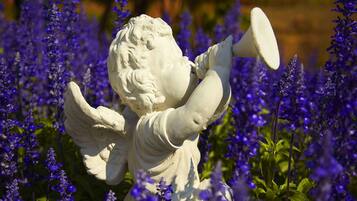 A statue of an angel with outstretched arms amidst purple flowers.