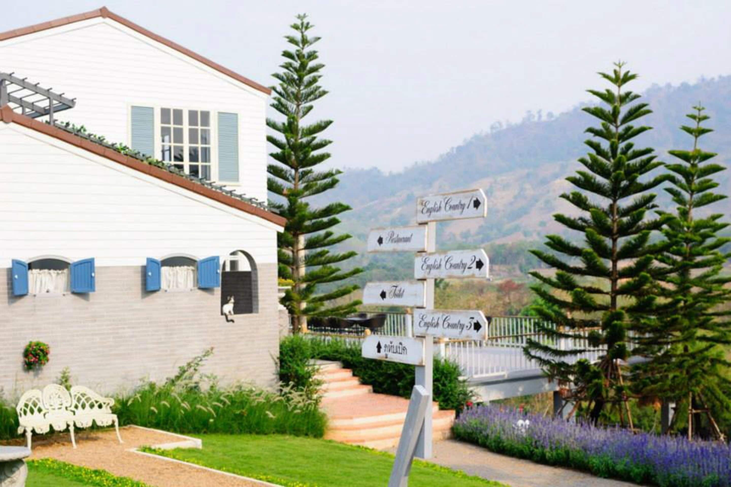 Un edificio blanco con contraventanas azules, un jardín con un banco blanco y señales indicativas para English Country y Restaurante.