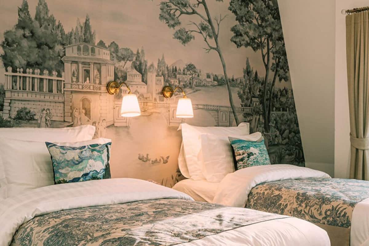 Une chambre d’hôtel avec deux lits, une fresque murale et deux lampes fixées au mur.
