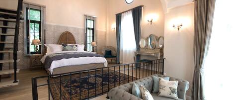 Un dormitorio amplio con una cama grande, una zona de estar con sofá, una escalera y una araña.