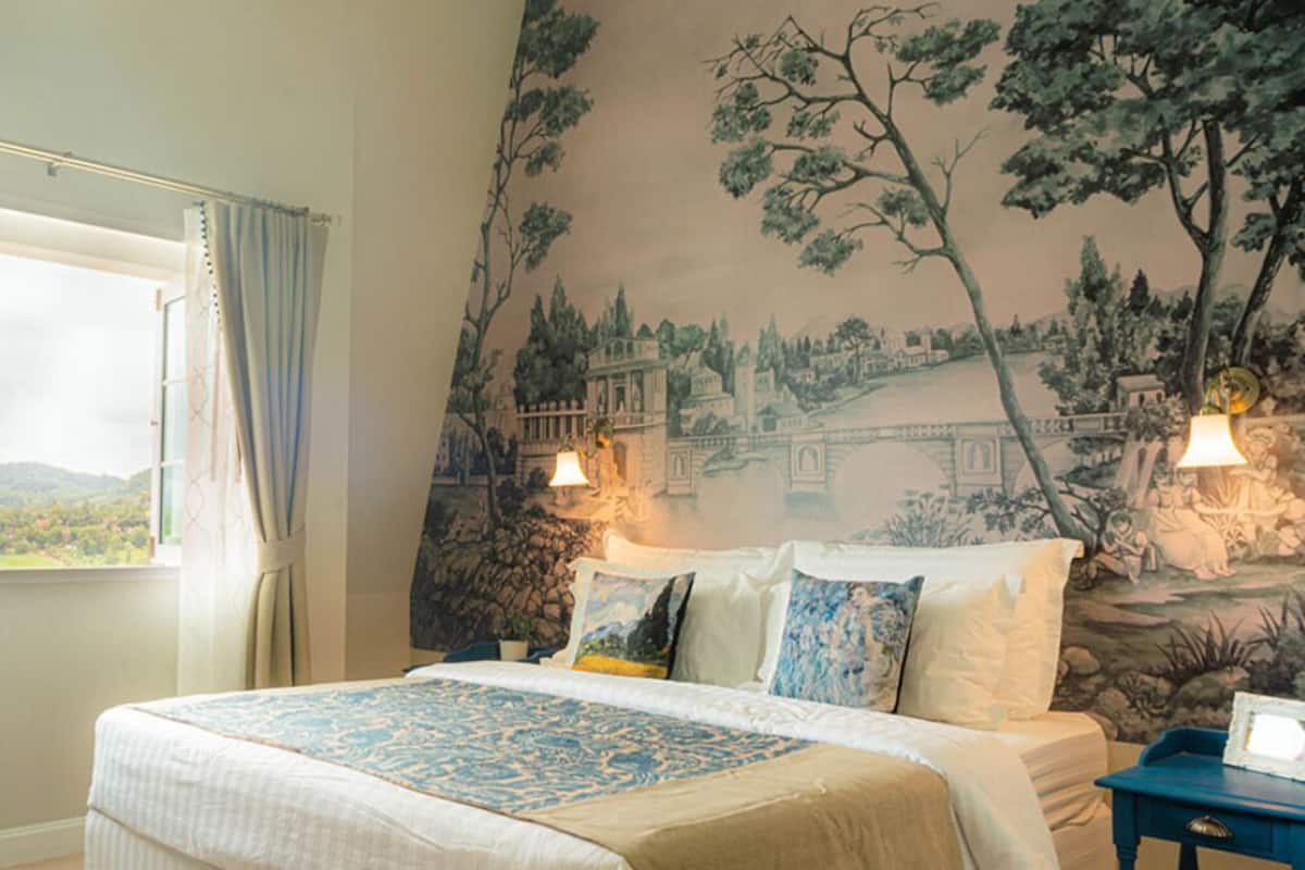 Une chambre avec un grand lit, une fresque murale et une fenêtre avec des rideaux.