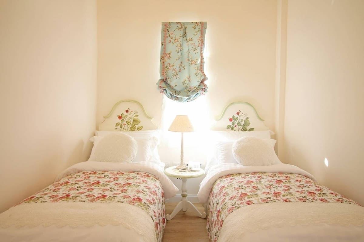 Une chambre avec deux lits, chacun agrémenté de draps à motifs floraux, une table de chevet avec une lampe et un rideau à motifs floraux.
