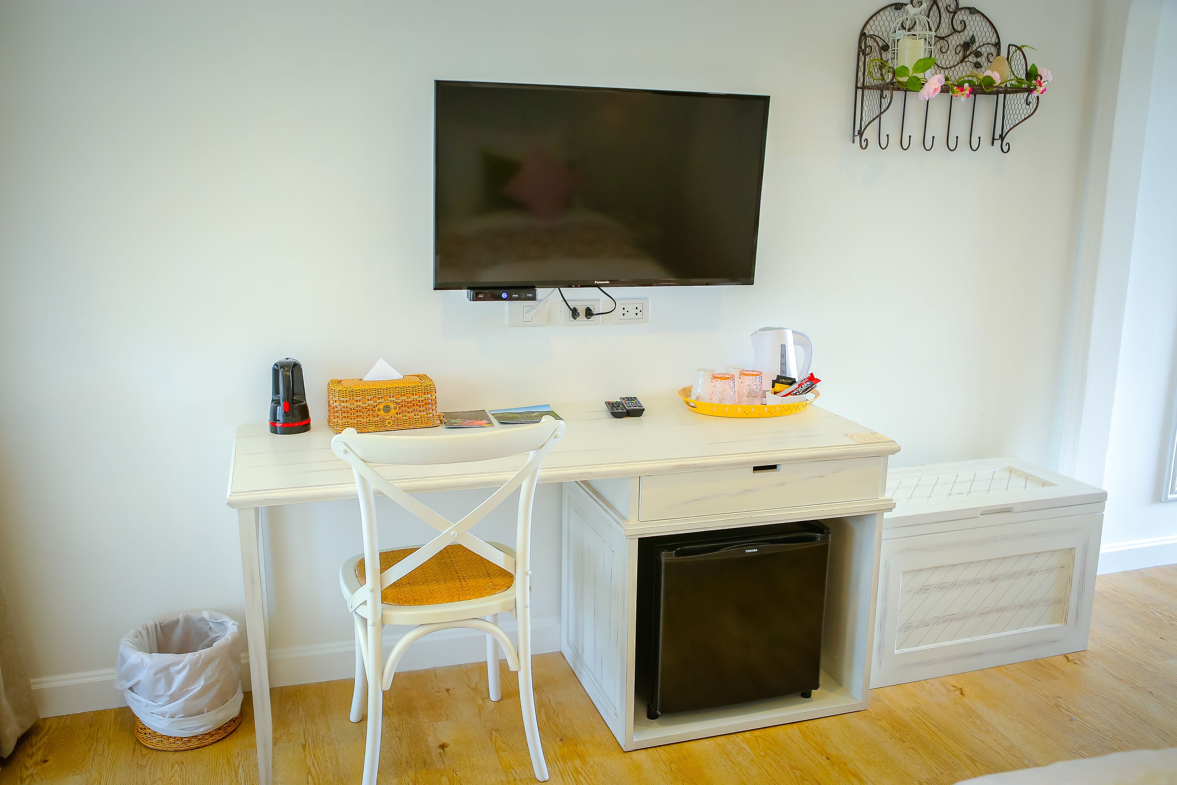 A compact kitchenette with a TV, a small fridge, a white chair, and a wicker basket.