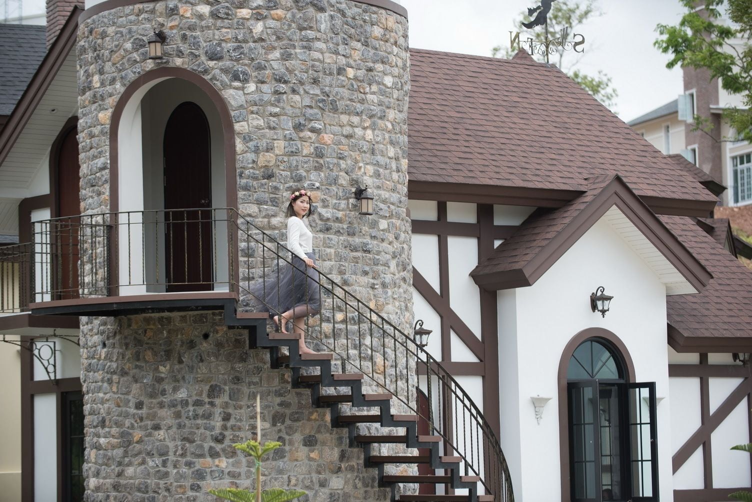 A stone tower with a staircase, a balcony, and a traditional building with a brown roof and white walls.