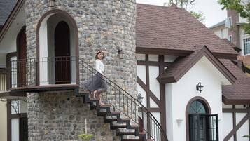 A stone tower with a staircase, a balcony, and a traditional building with a brown roof and white walls.