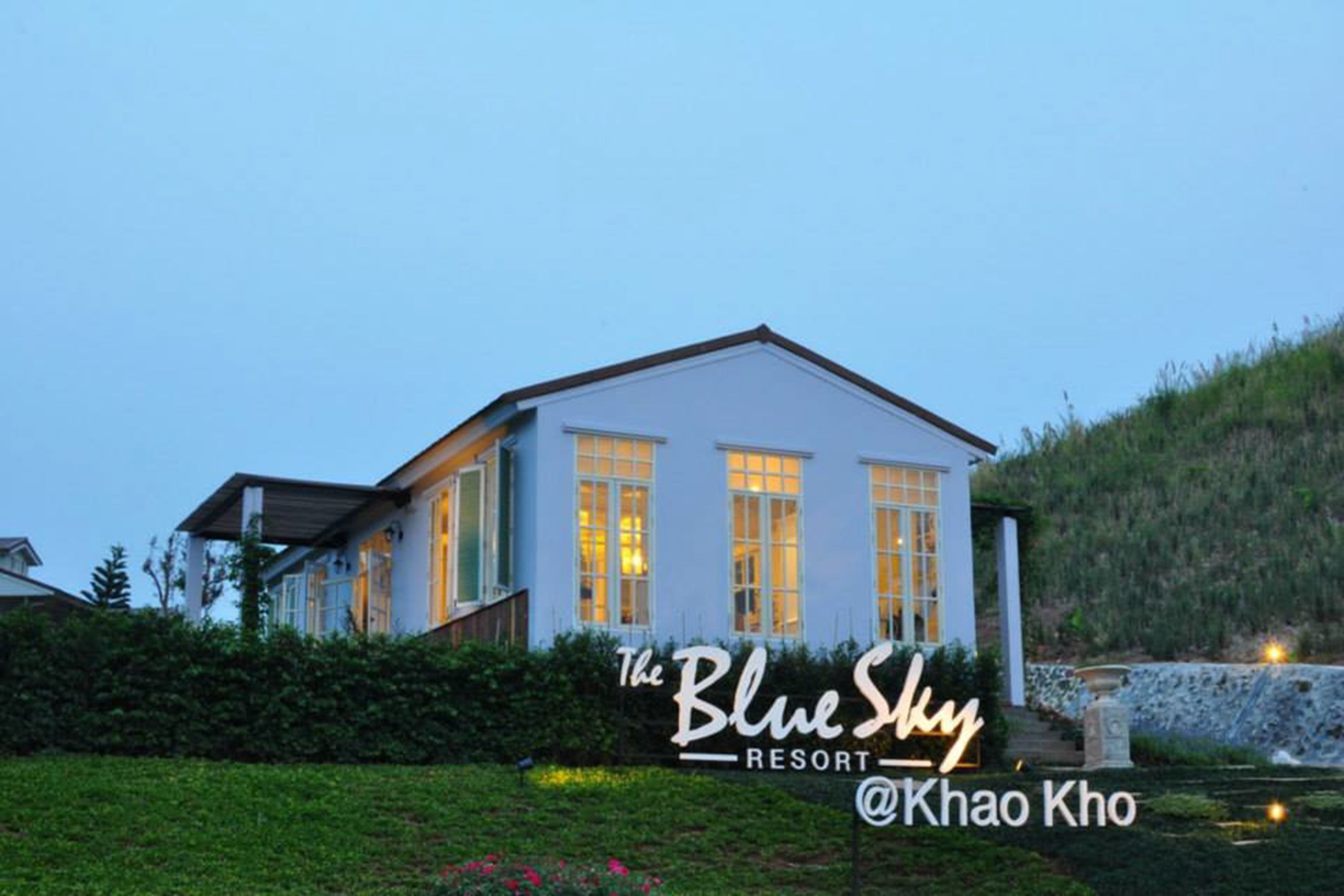 The Blue Sky Resort with a white exterior, large windows, and a stone wall in the background.