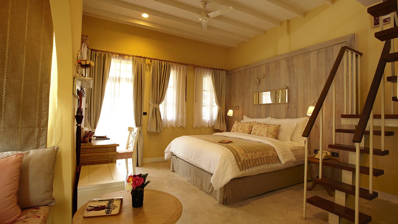 A bedroom with a bed, a nightstand, a chair, a table with a vase of flowers, and a wooden ladder.
