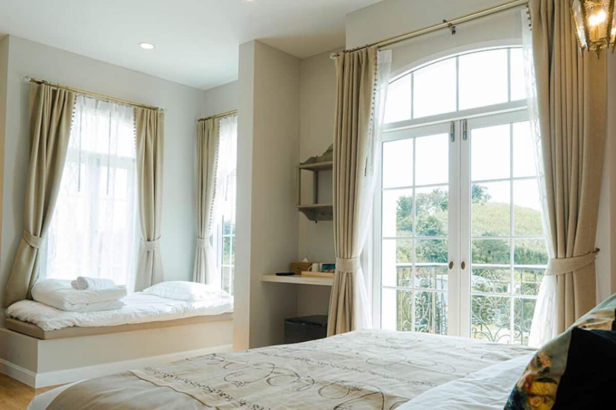 Une chambre avec un grand lit, une fenêtre avec des rideaux, une table de chevet et une vue sur la verdure.