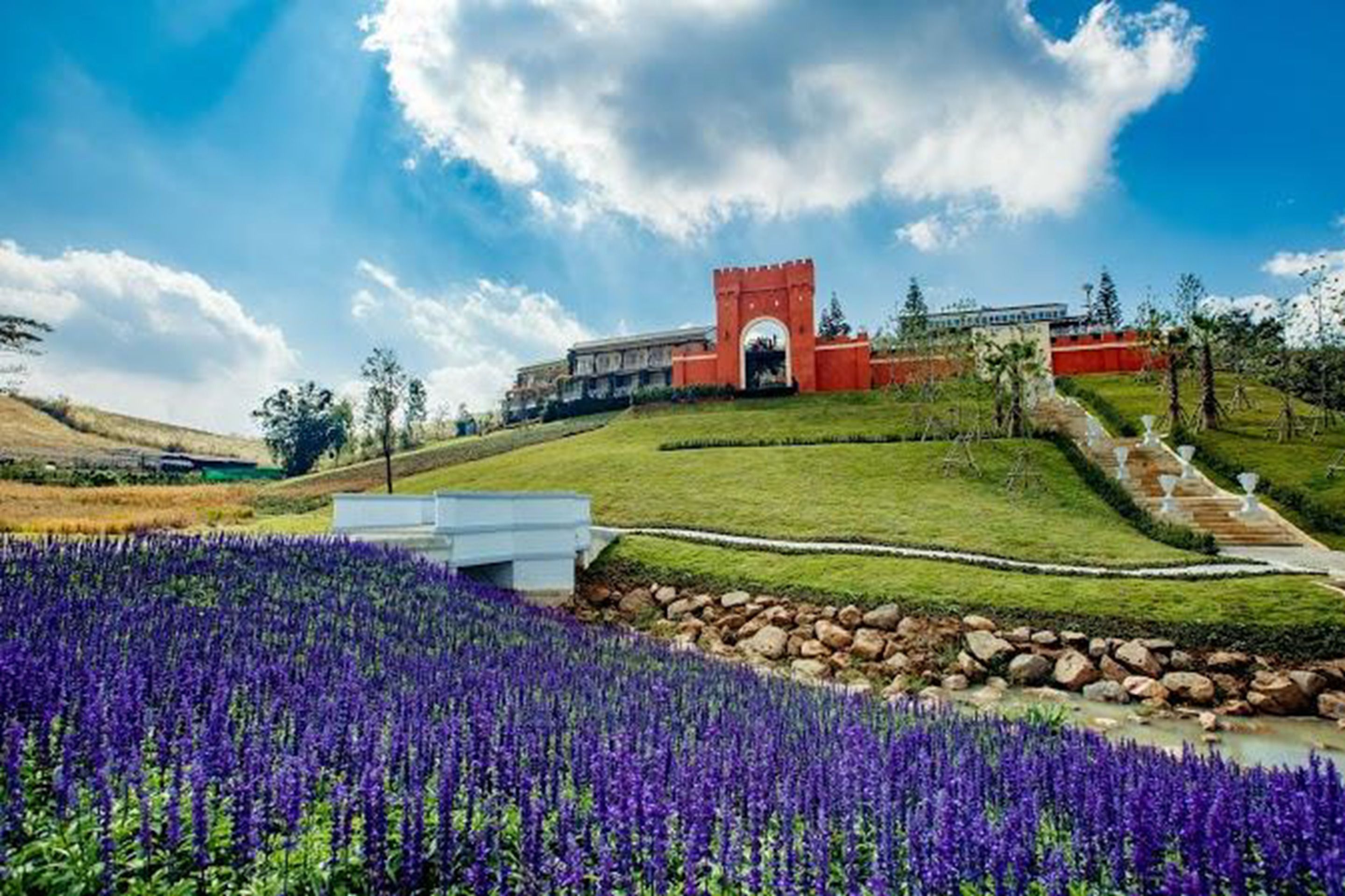 Un edificio con un arco rojo, rodeado de un césped cuidado y flores moradas.