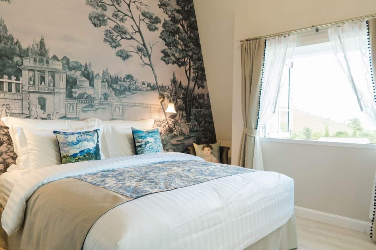 Une chambre à coucher avec un lit, une grande fresque murale, une fenêtre avec des rideaux et une table de chevet avec une lampe.