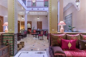 Un vestíbulo amplio con techo alto, columnas ornamentales y una zona de estar central con sofá y sillones.