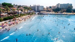 A beach with people swimming and sunbathing, a hotel named 'HOTEL MARTI' in the background, and a clear blue sea. - Marti Beach Hotel (Kusadasi)