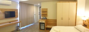 Een hotelkamer met een bed, een aan de muur bevestigde televisie, een minibar, een kledingkast en een klein zithoekje met een bankje.