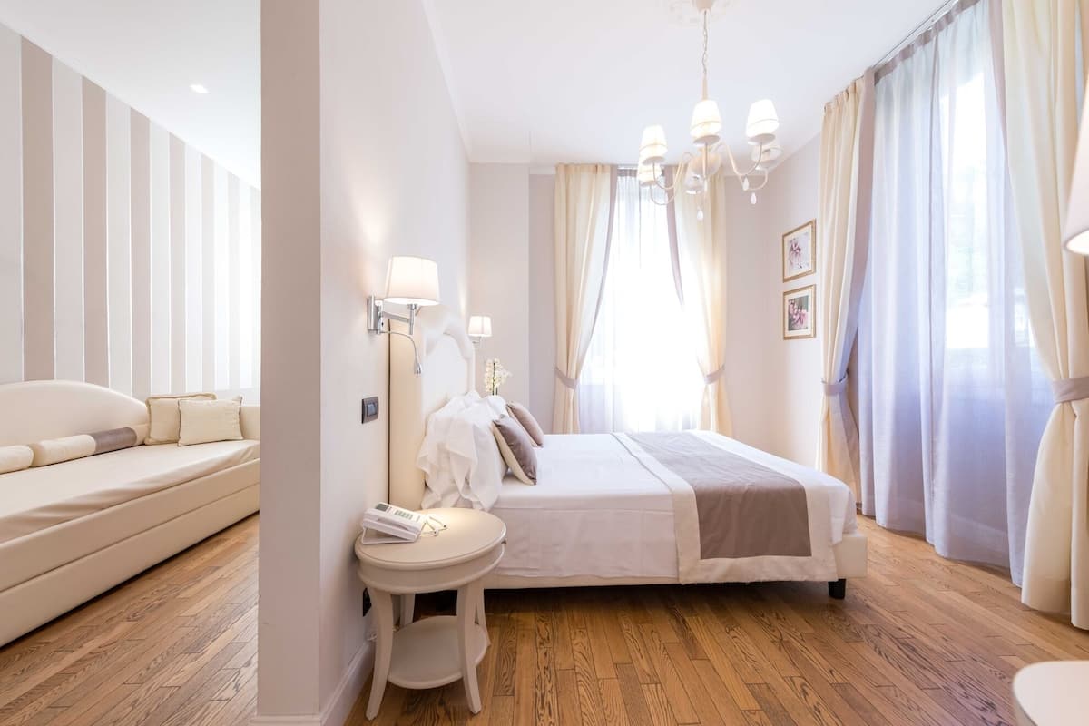 Une chambre d’hôtel avec un grand lit, une table de chevet, un canapé et un lustre.
