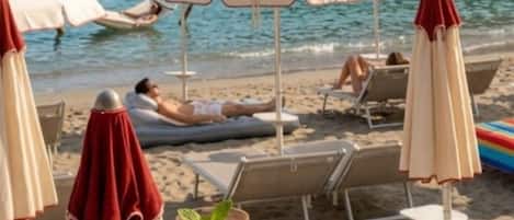 Eine Strandlounge mit Liegestühlen, Sonnenschirmen und einem Getränk mit Trinkhalm.