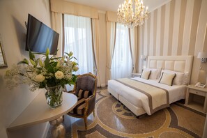 A hotel room with a bed, a TV mounted on the wall, a vase with flowers, a chair, and a carpeted floor. - Hotel Sant'Andrea (Santa Margherita Ligure)