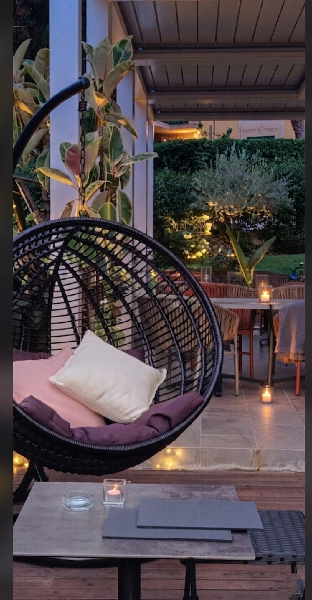 Un'area salotto esterna con una sedia in vimini, un tavolo con una candela e vista su un giardino.