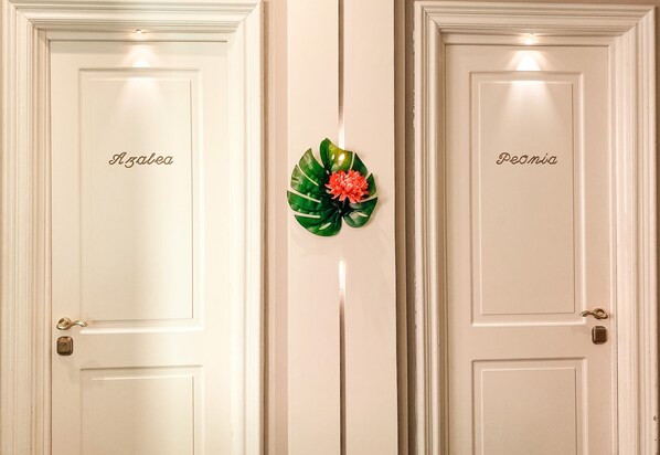 Two white doors with names "Azalea" and "Peanias" on them, separated by a decorative green leaf with a red flower. - Hotel Sant'Andrea (Santa Margherita Ligure)