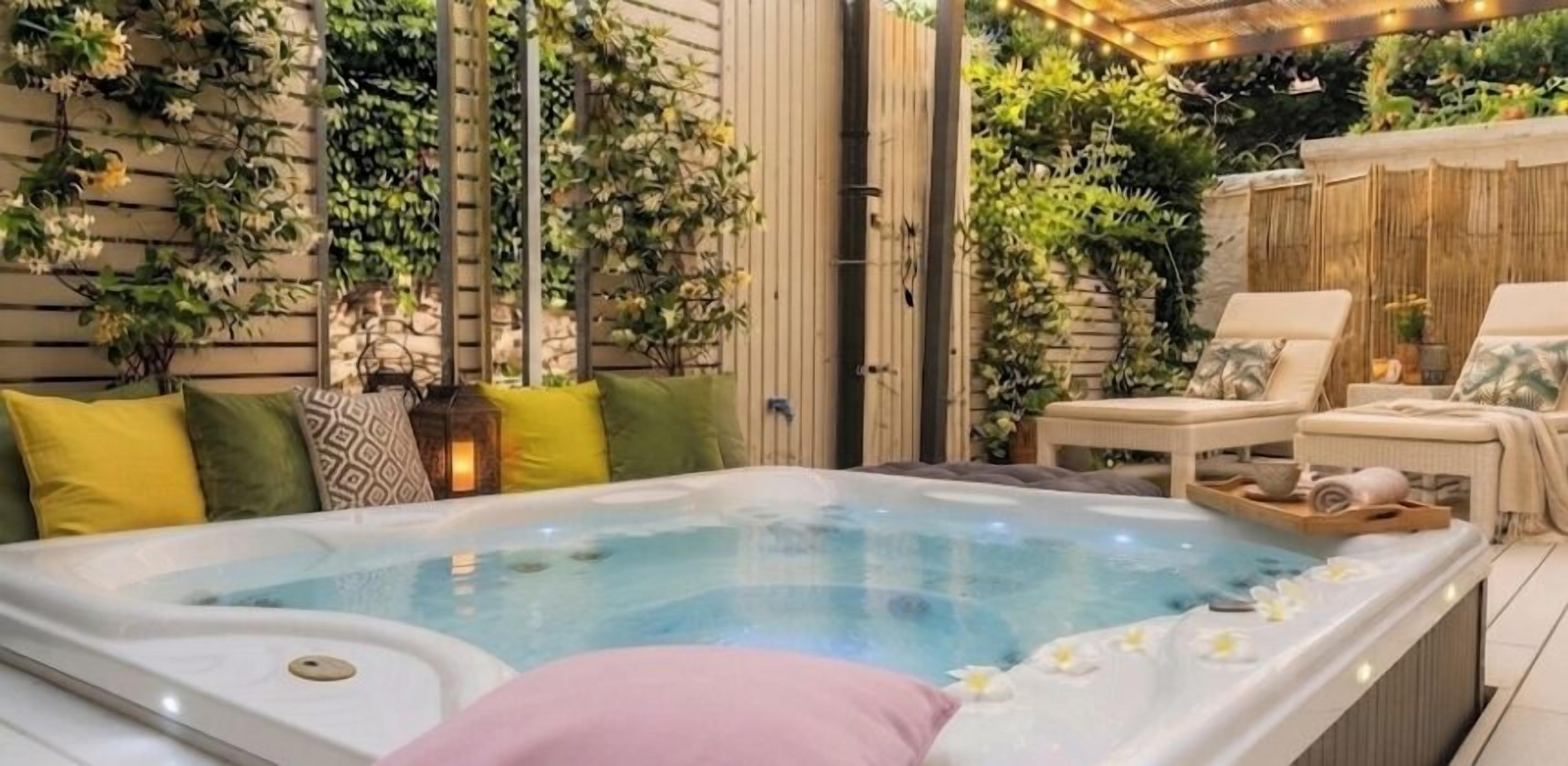 A hot tub with a wooden deck, surrounded by greenery and a bamboo fence.