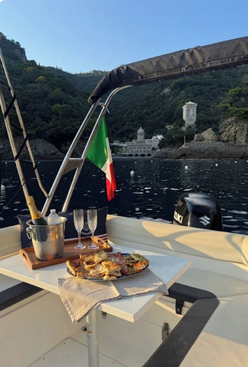 A boat with a table set for a meal, a flag, and a view of a bridge and hills.
