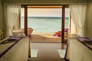 Um quarto com duas camas, uma banheira e vista para o mar.