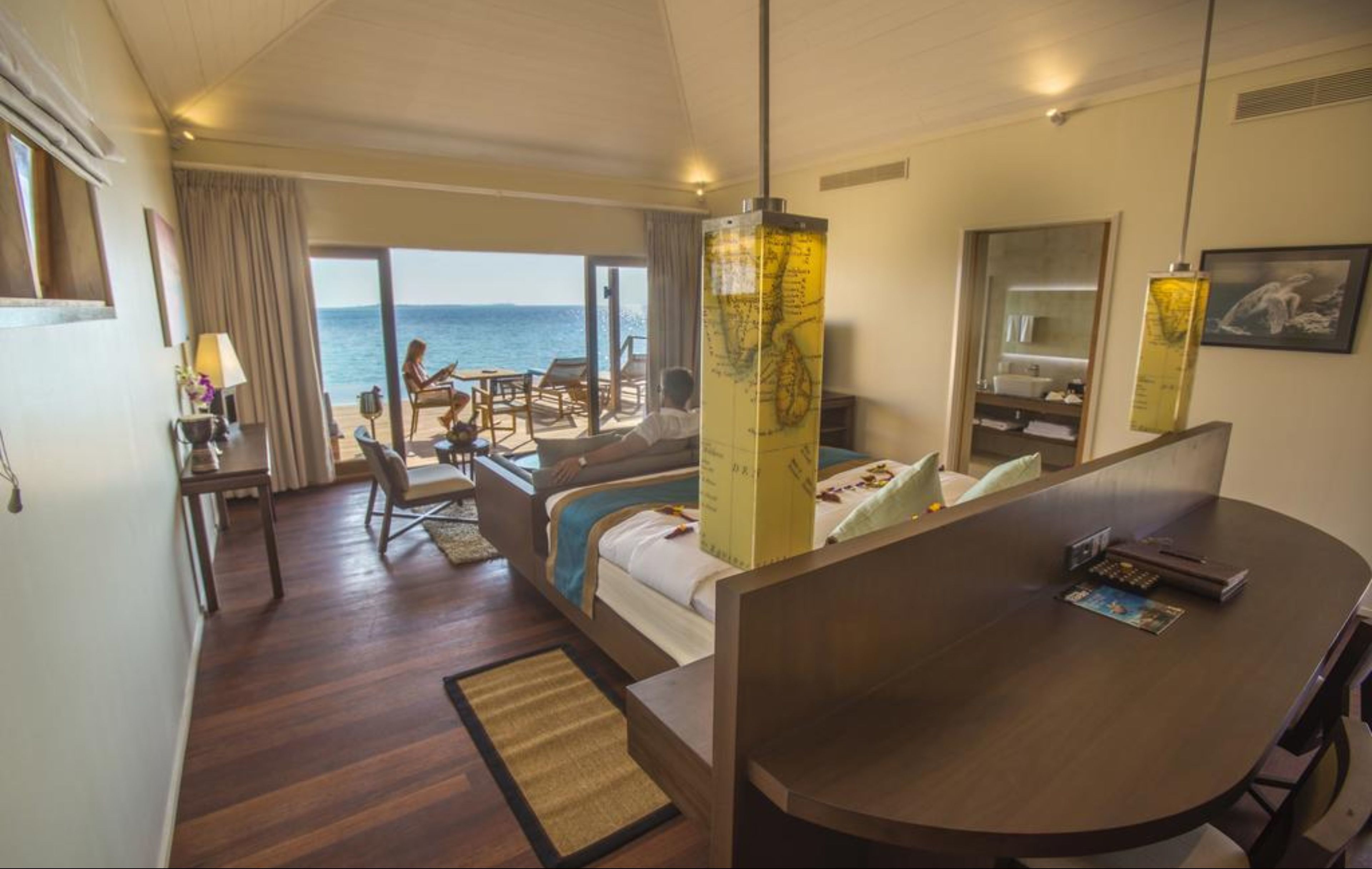 A hotel room with a bed, a desk, a chair, a sofa, and a view of the sea.