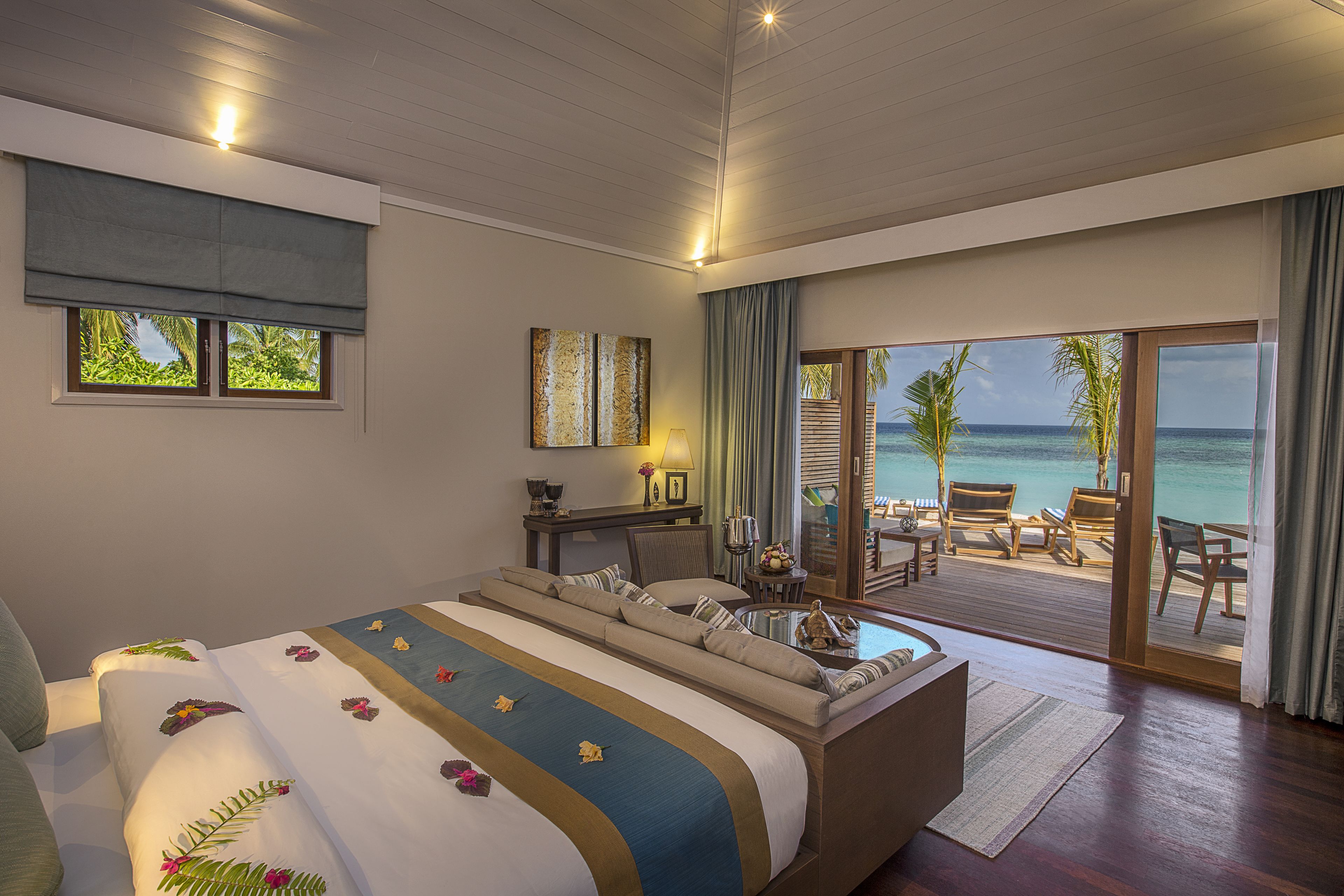 A bedroom with a bed, a sofa, a desk, and a view of the ocean.