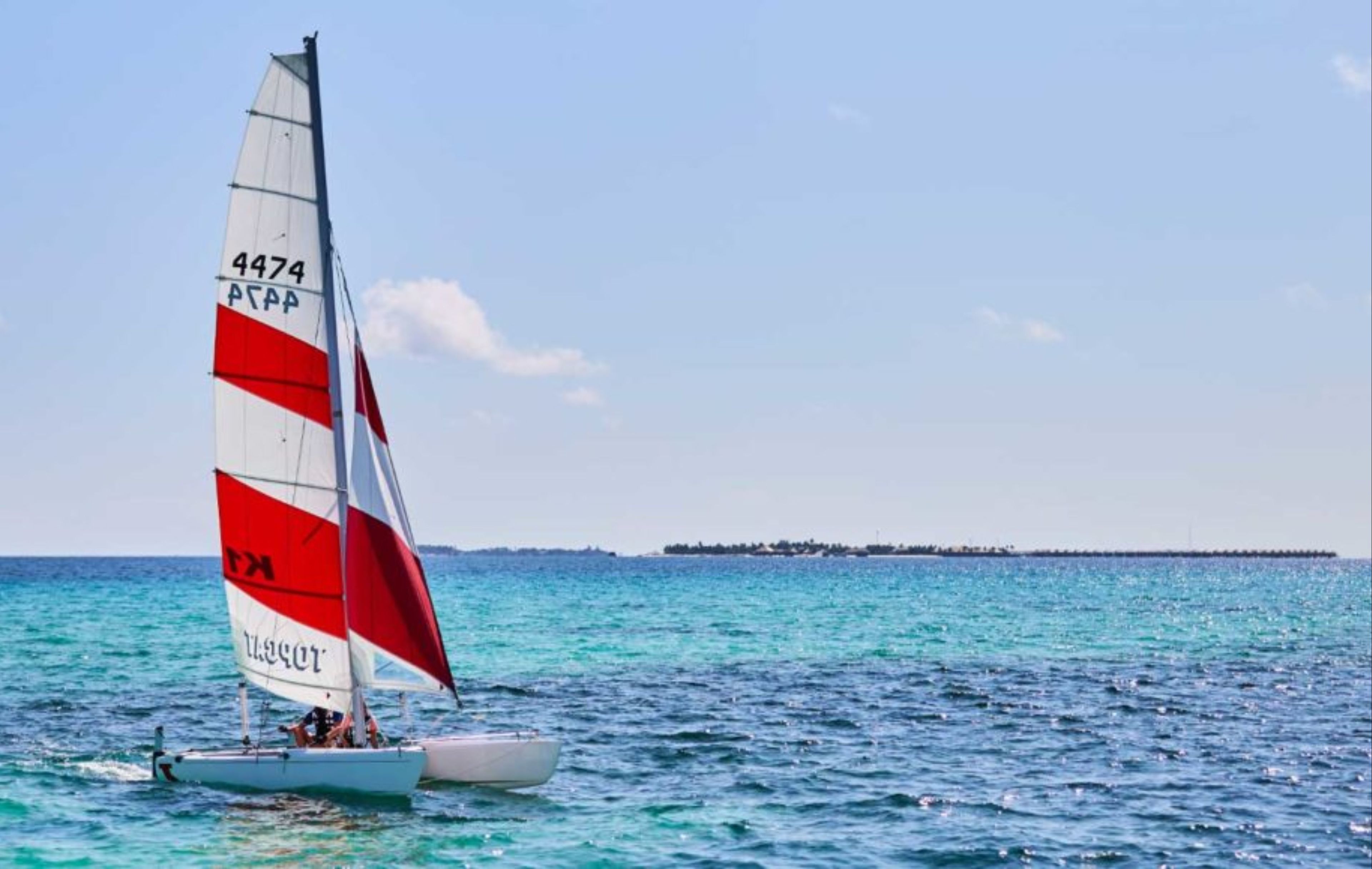 Un voilier avec une voile rouge et blanche sur une mer calme.
