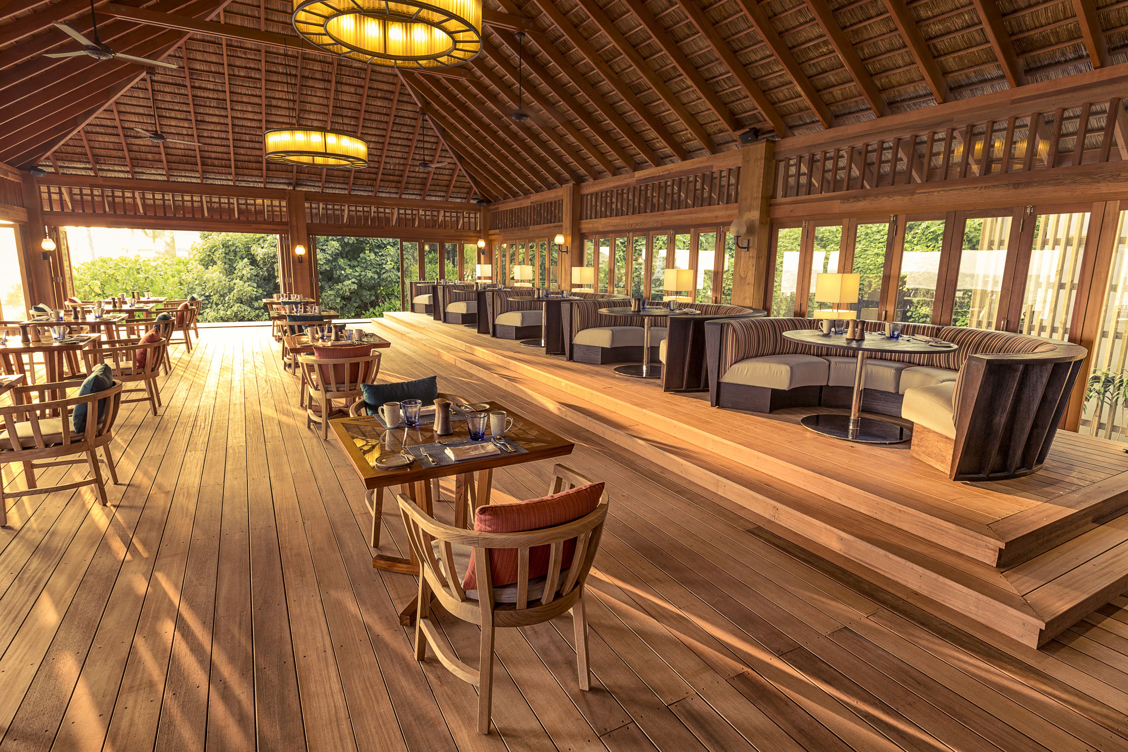 Un vaste espace extérieur aménagé pour les repas, doté d’un plancher en bois et de sièges, ainsi que de grandes fenêtres offrant une vue sur la verdure environnante.