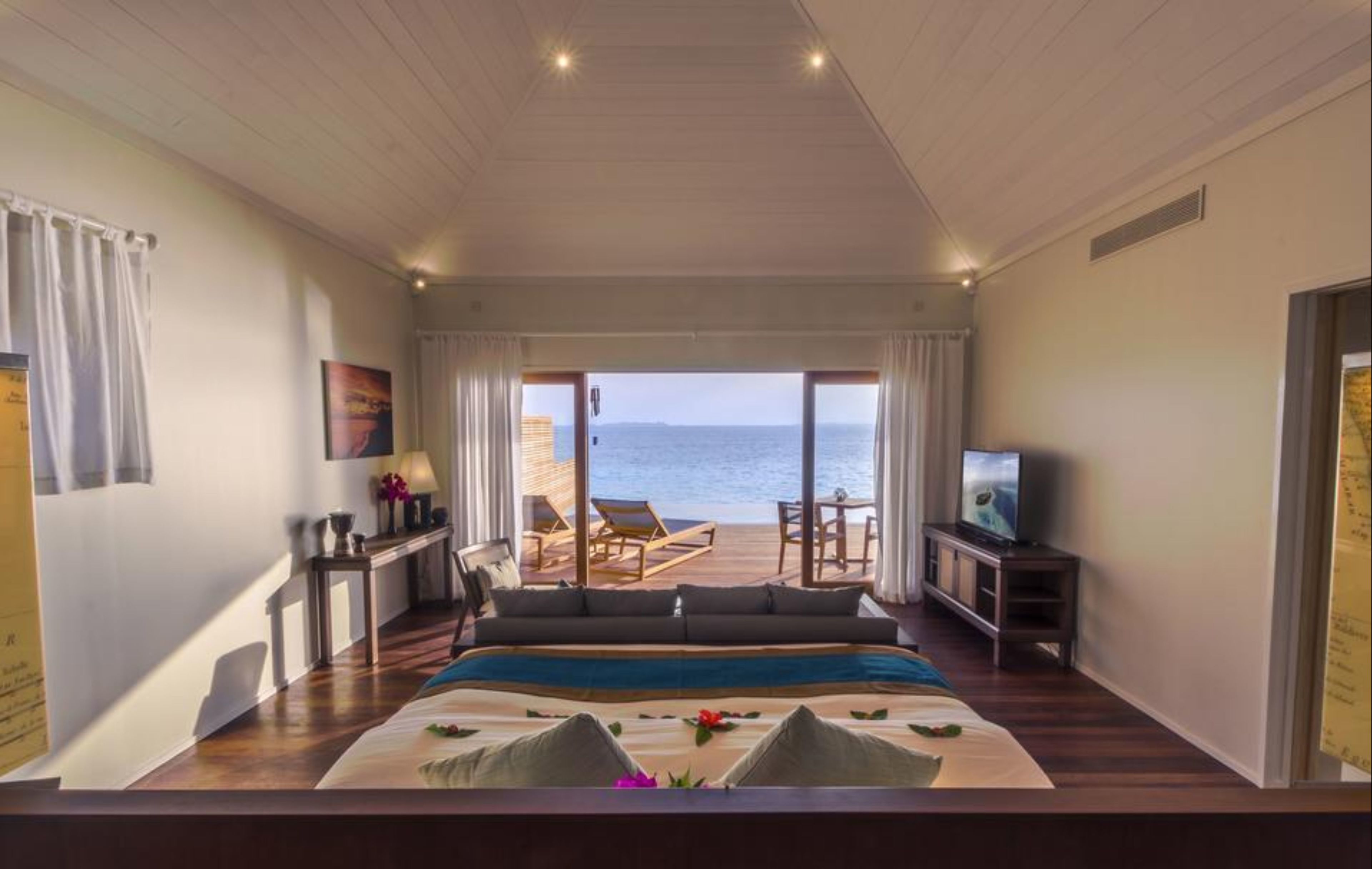 A bedroom with a large bed, a TV, and a view of the sea.