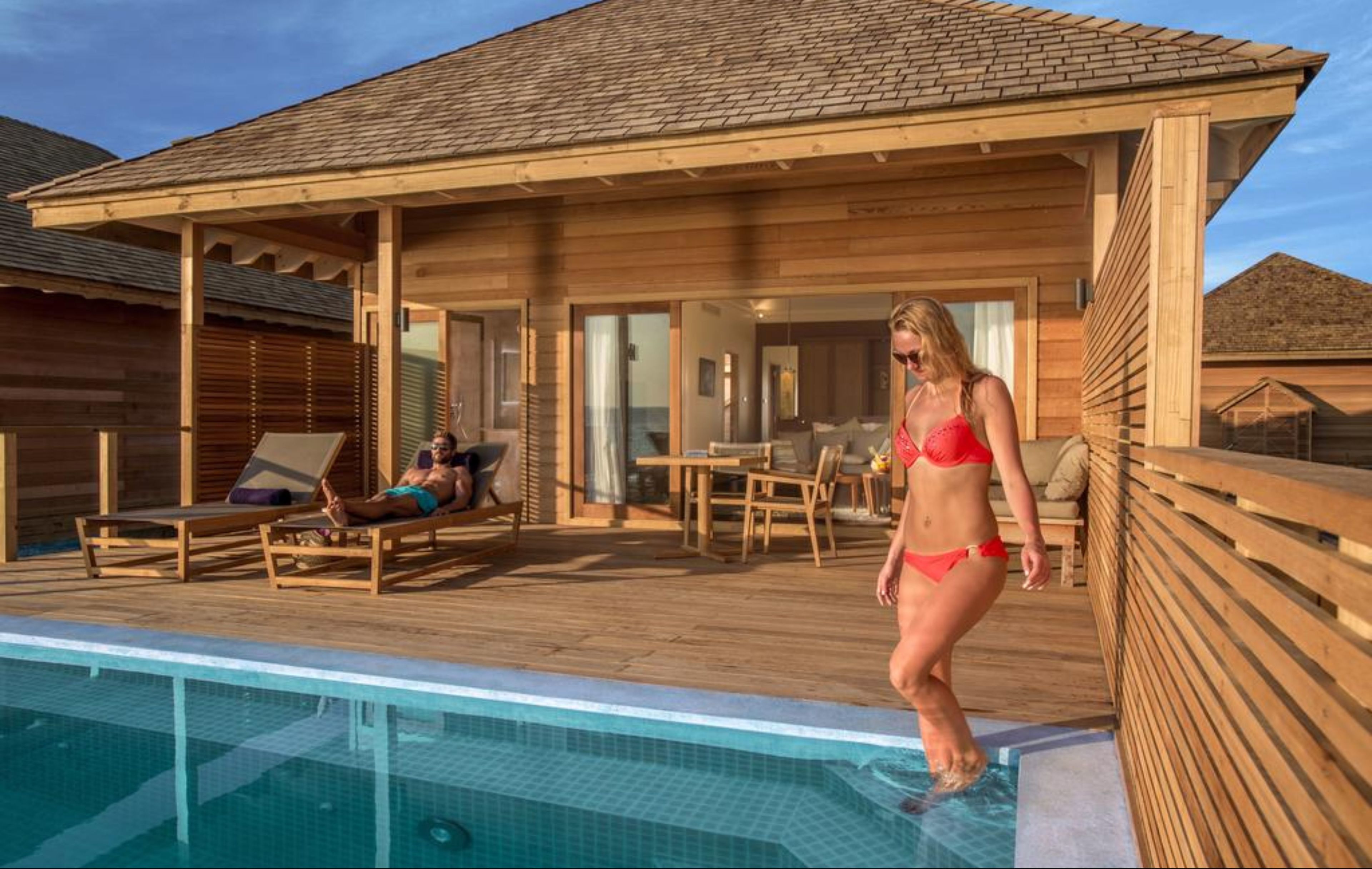 A wooden deck with a pool, lounge chairs, and a covered seating area.