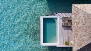 Vue aérienne d’une piscine à débordement moderne, dotée d’une terrasse en bois et d’un espace détente.