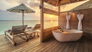 Une terrasse en bois avec une grande baignoire, des chaises longues et un parasol.