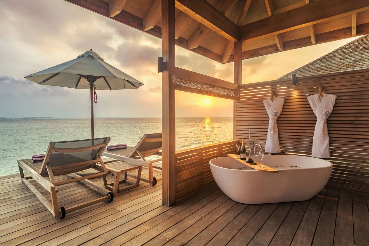 Een houten terras met een groot bad, lounge stoelen en een parasol.