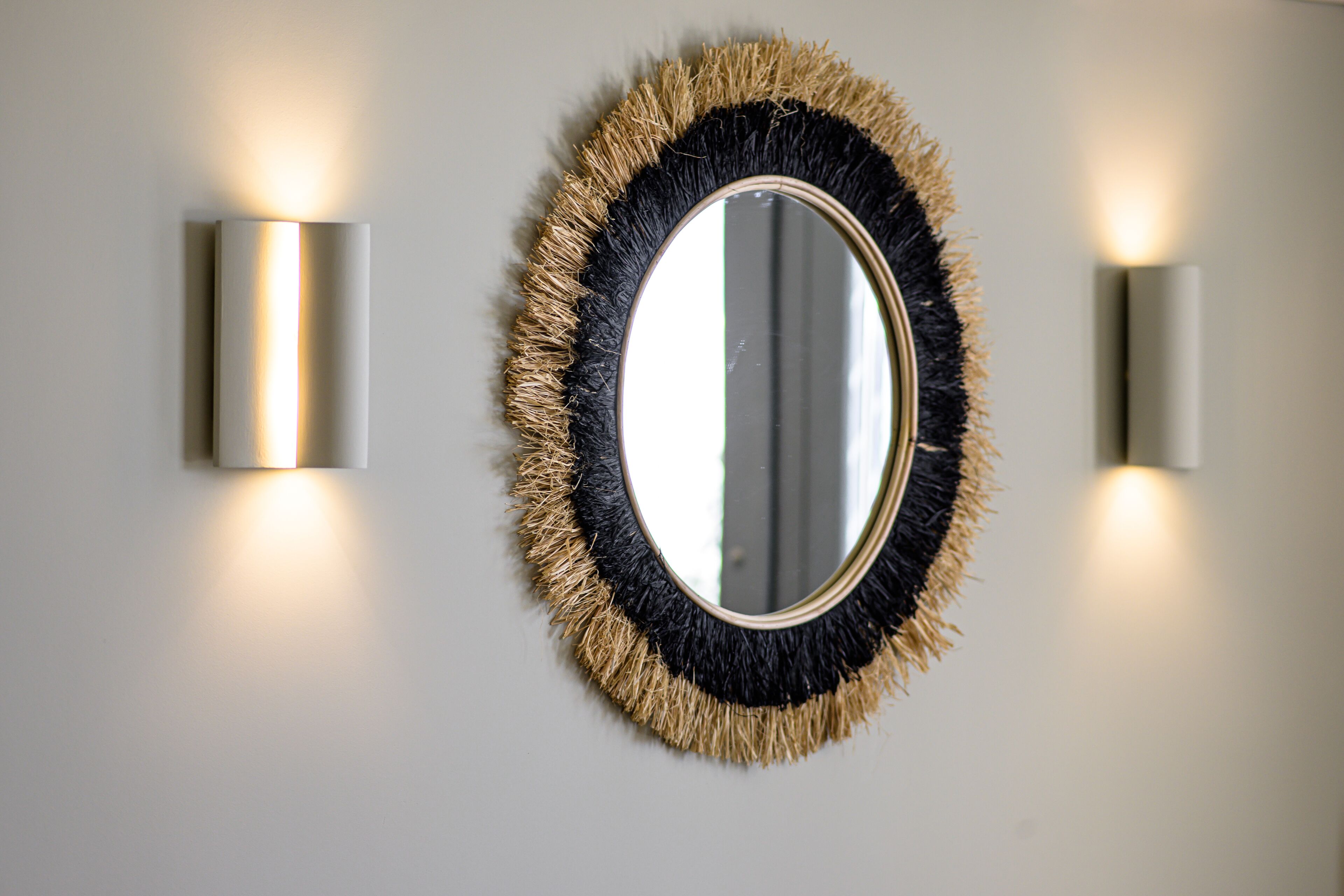 A wall-mounted mirror with a textured frame and two wall sconces on either side.
