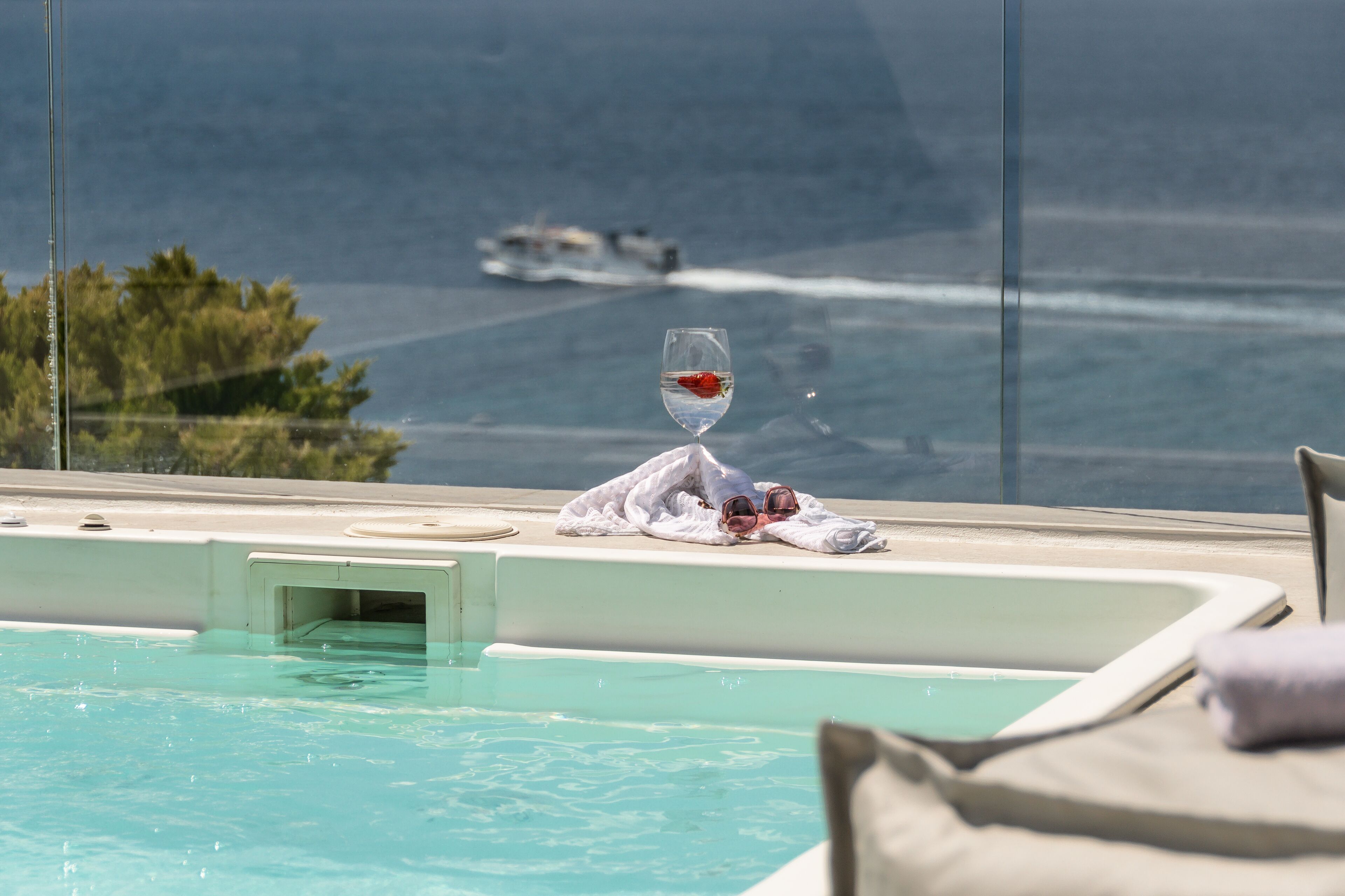 A pool with a glass of water and a towel on the edge, overlooking a body of water with a boat in the distance.