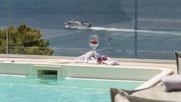 A pool with a glass of water and a towel on the edge, overlooking a body of water with a boat in the distance.