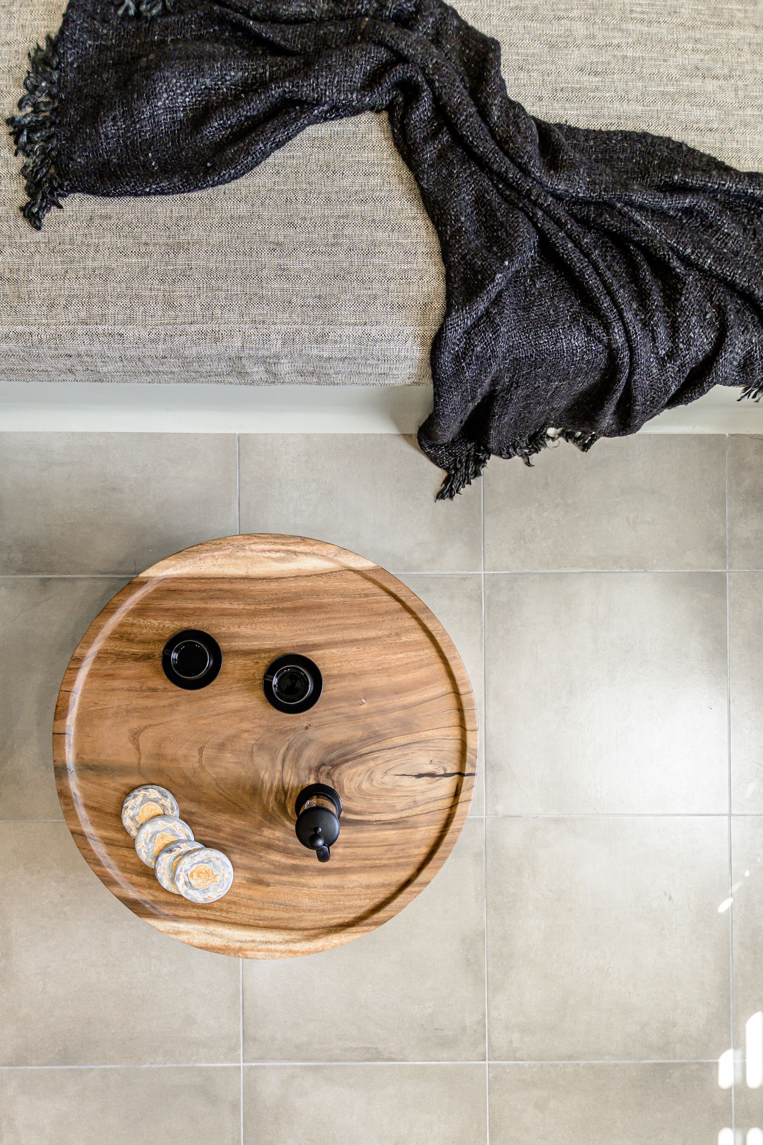 A round wooden table with two black handles and a bottle on it, placed on a tiled floor.