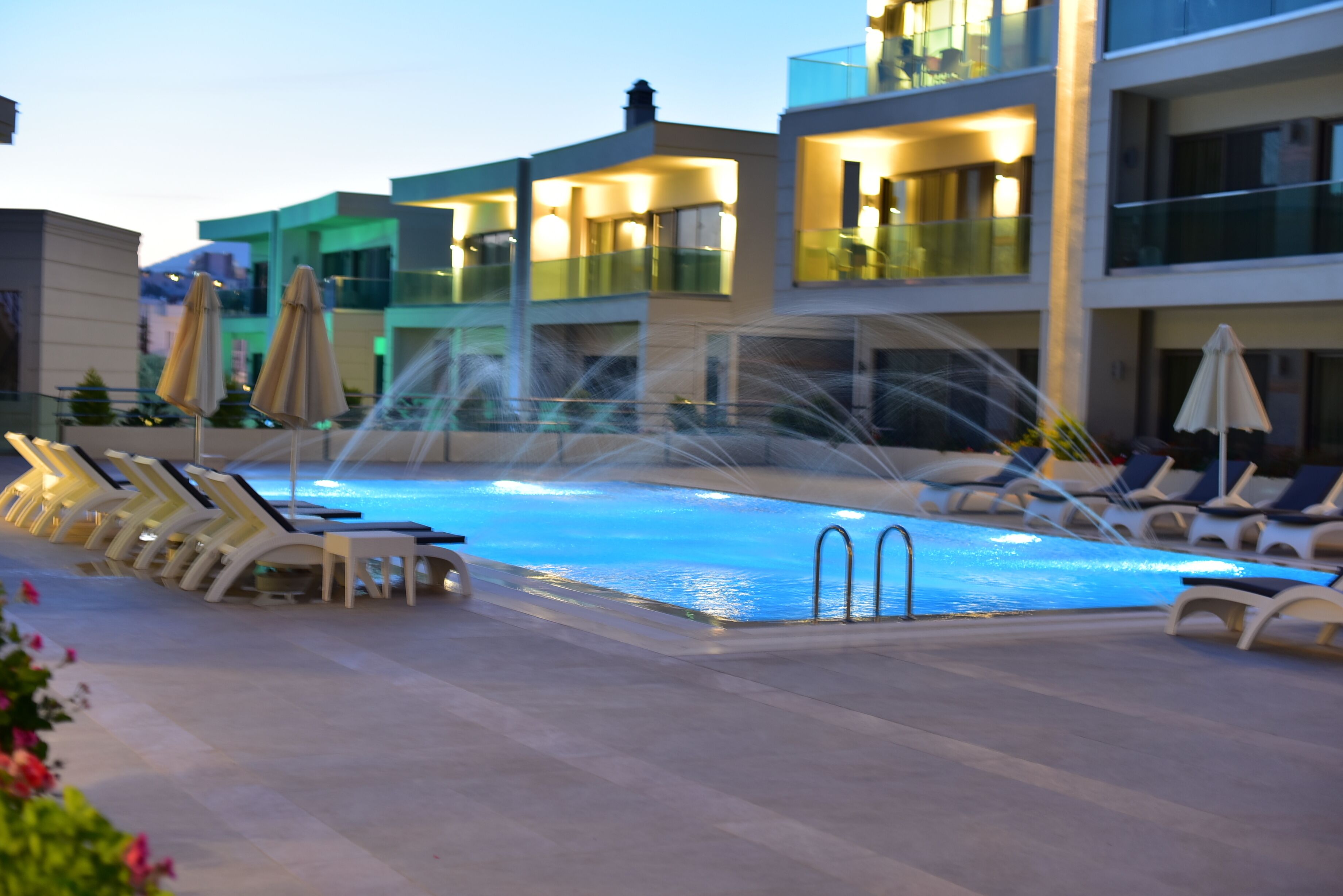 A swimming pool with lounge chairs and umbrellas, surrounded by multi-story buildings with balconies.