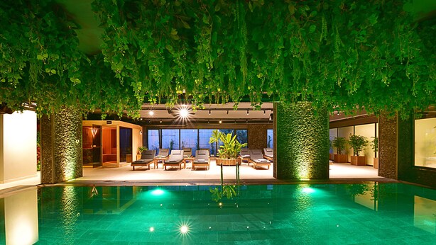 An indoor swimming pool with a sunlit lounge area, surrounded by greenery and modern architecture. - Jasmin Elite Residence & SPA (Bodrum)