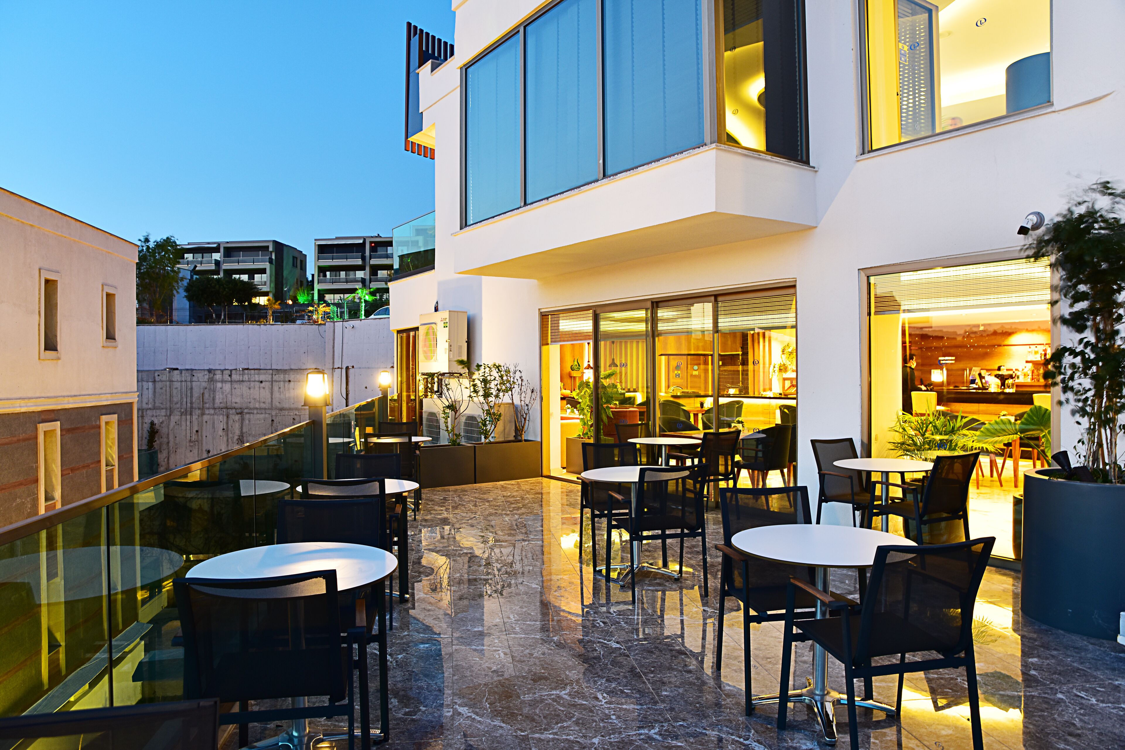 A modern outdoor dining area with glass railings, multiple tables, and chairs.