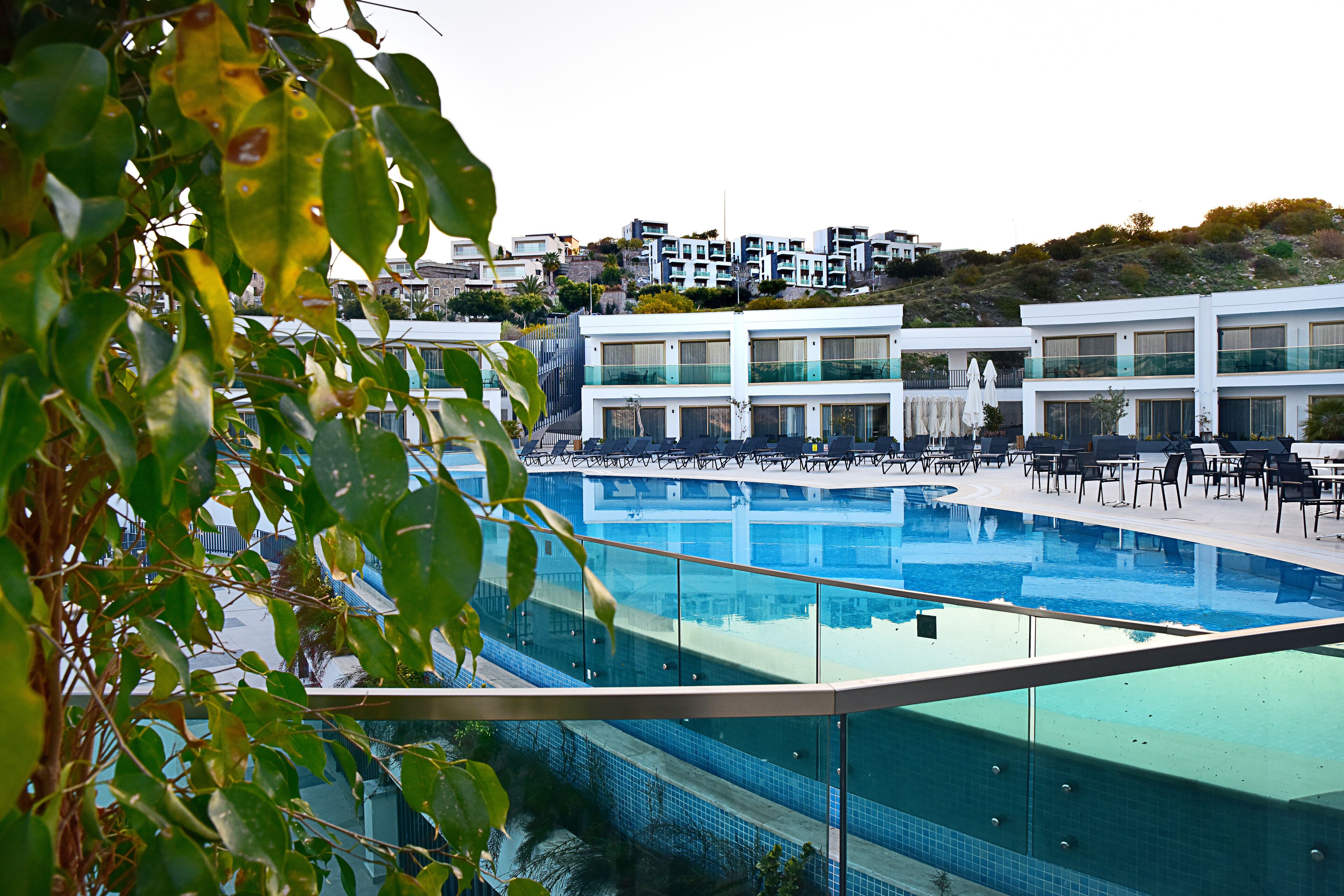 A modern hotel with a large pool, multiple balconies, and a view of the surrounding hillside.