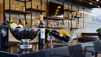 Un coin bar avec des étagères remplies de bouteilles d’alcool, un grand saladier de fruits et une bouteille de vin posée sur le comptoir.