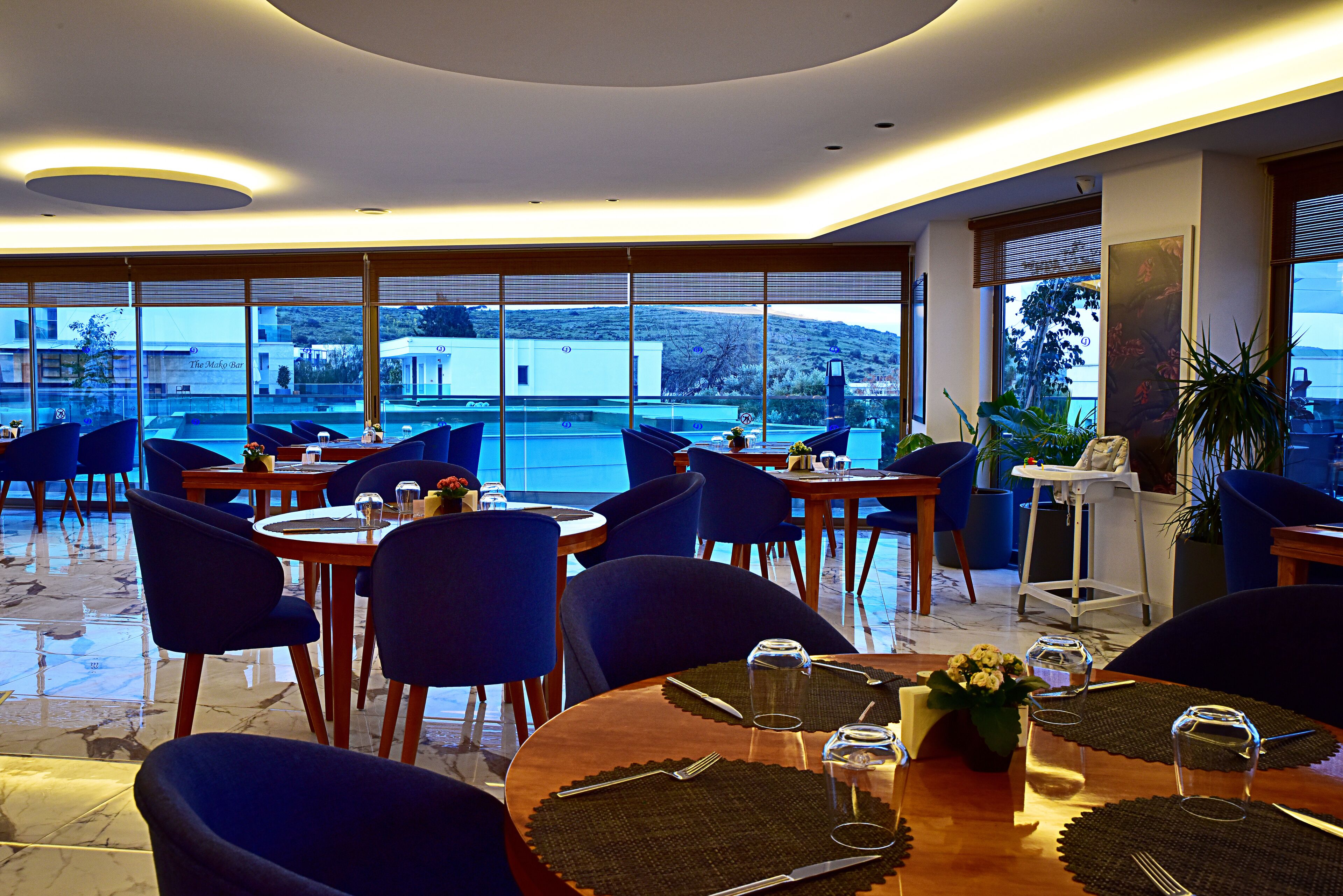 Un restaurant avec des tables rondes, des chaises bleues et une vue sur un plan d’eau.