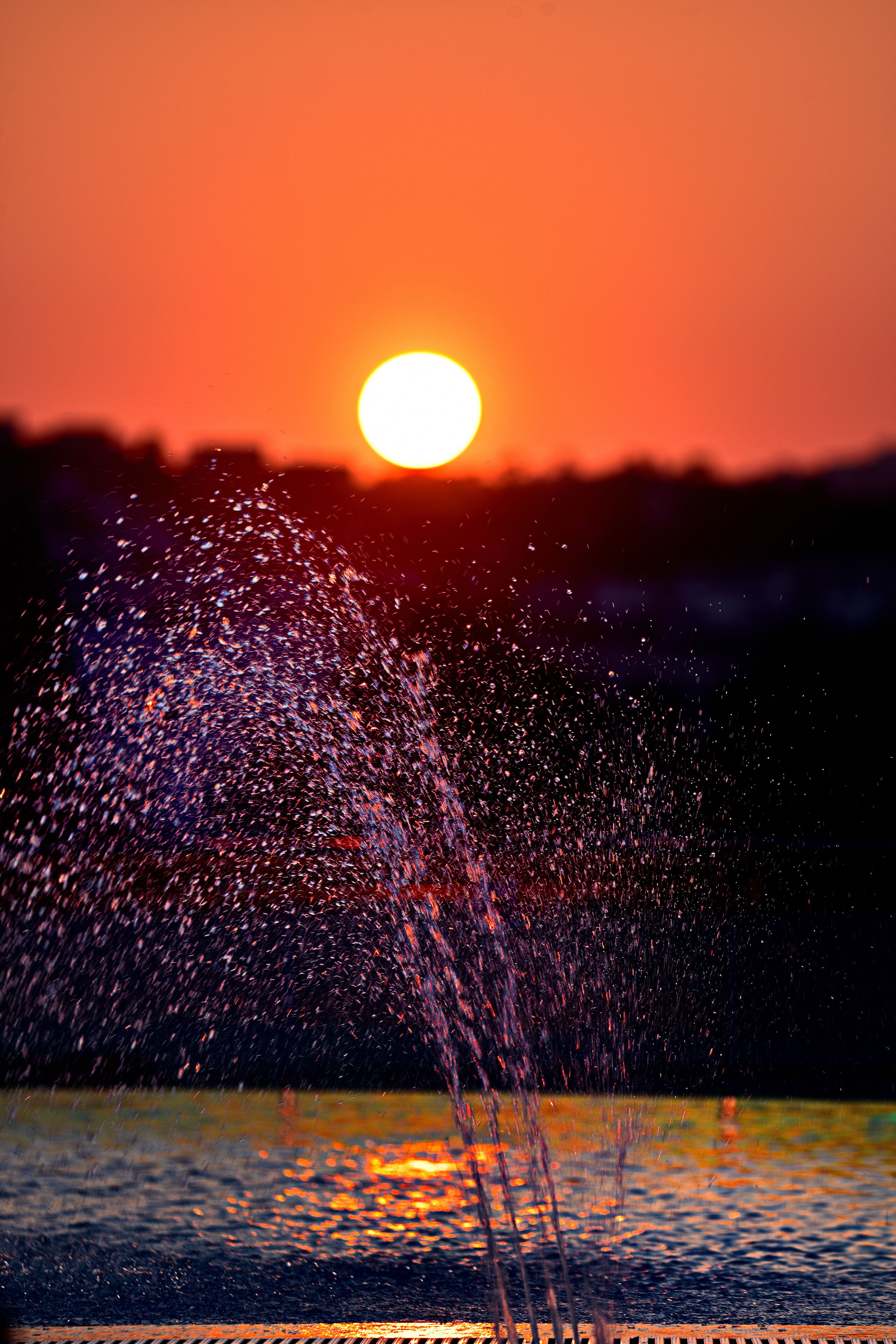 Un coucher de soleil sur une étendue d’eau, avec une fontaine.