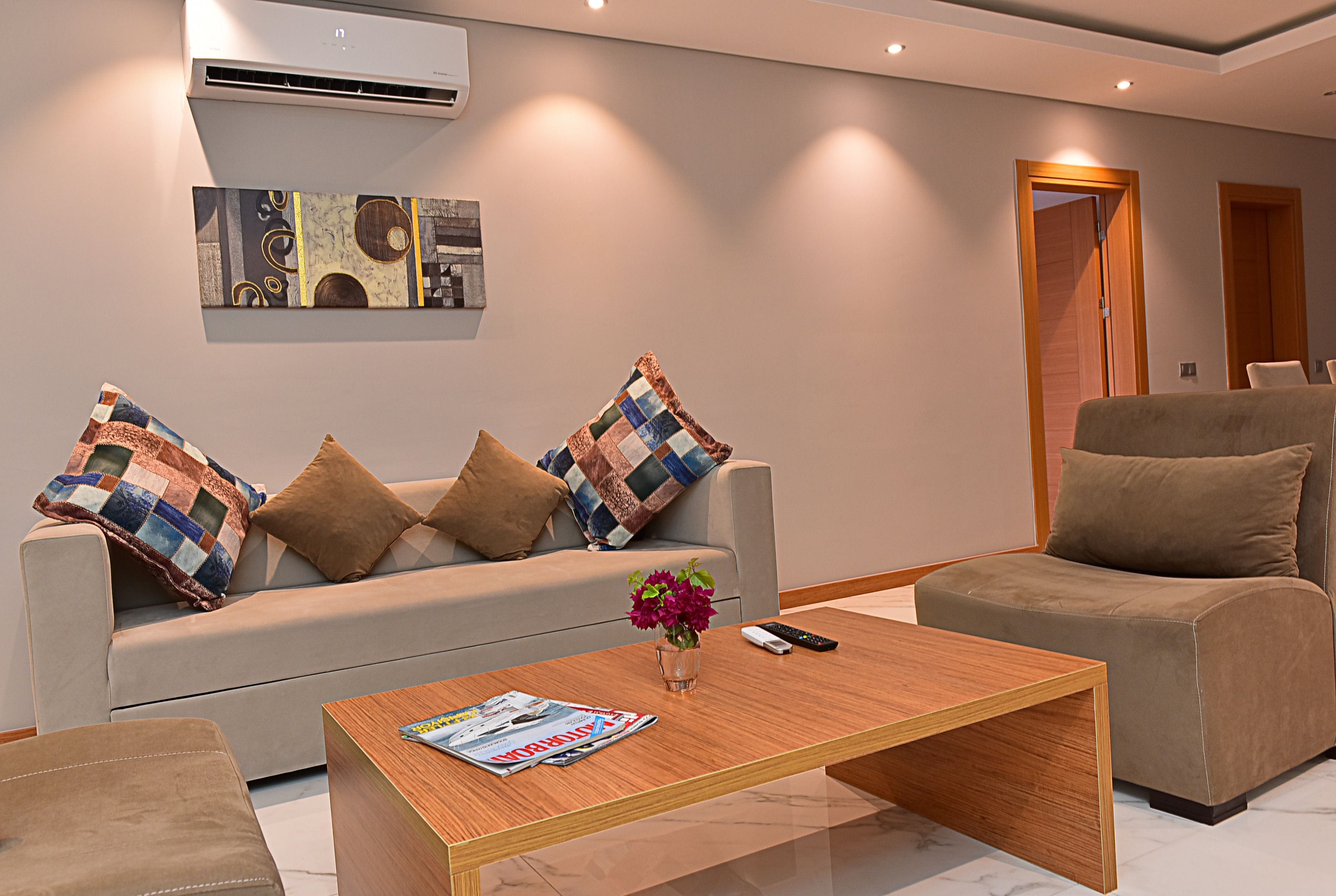 Una sala de estar moderna con un sofá, dos sillones, una mesita de centro y un aire acondicionado instalado en la pared.