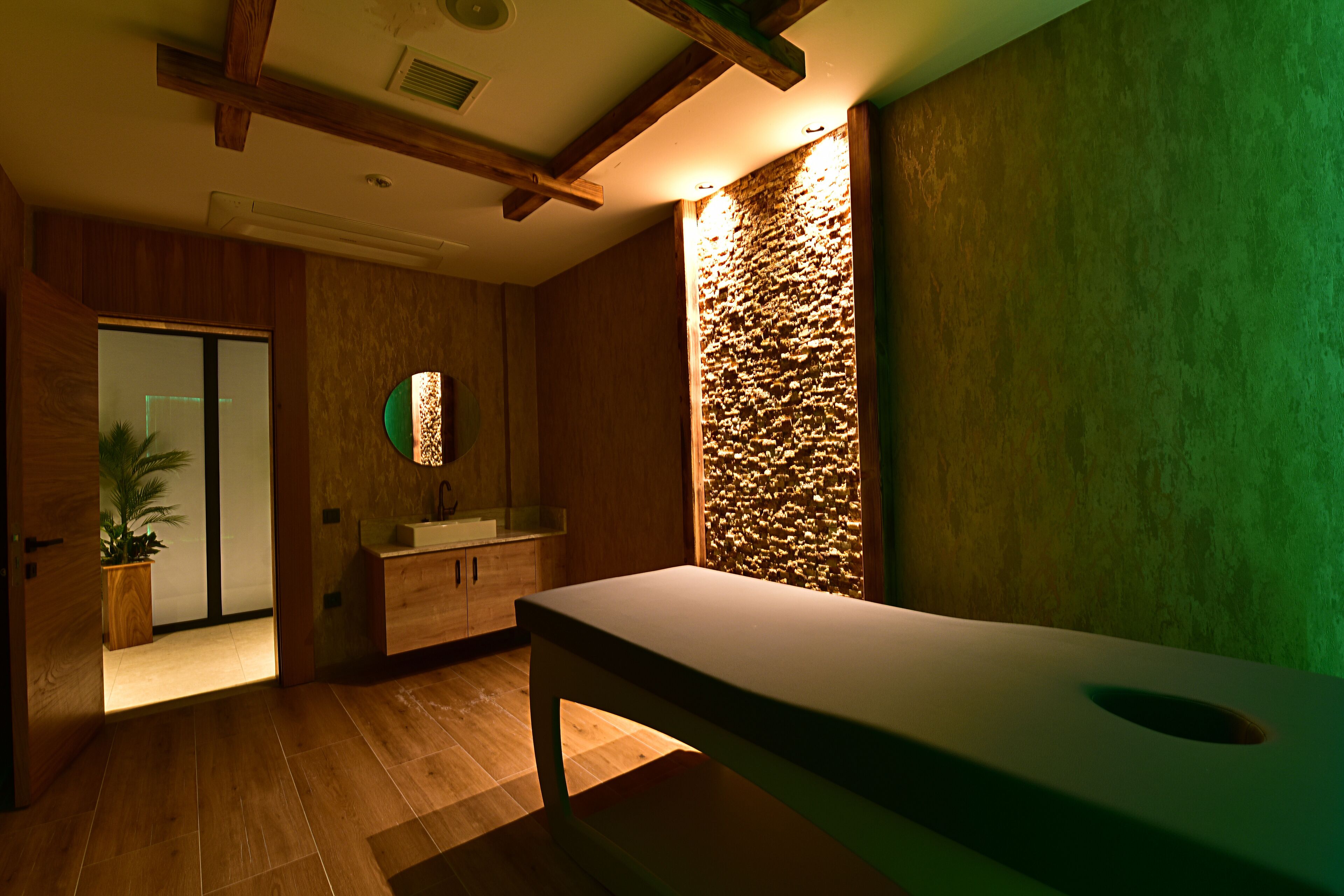 A modern bathroom with wooden flooring, a large sink, and a stone accent wall.