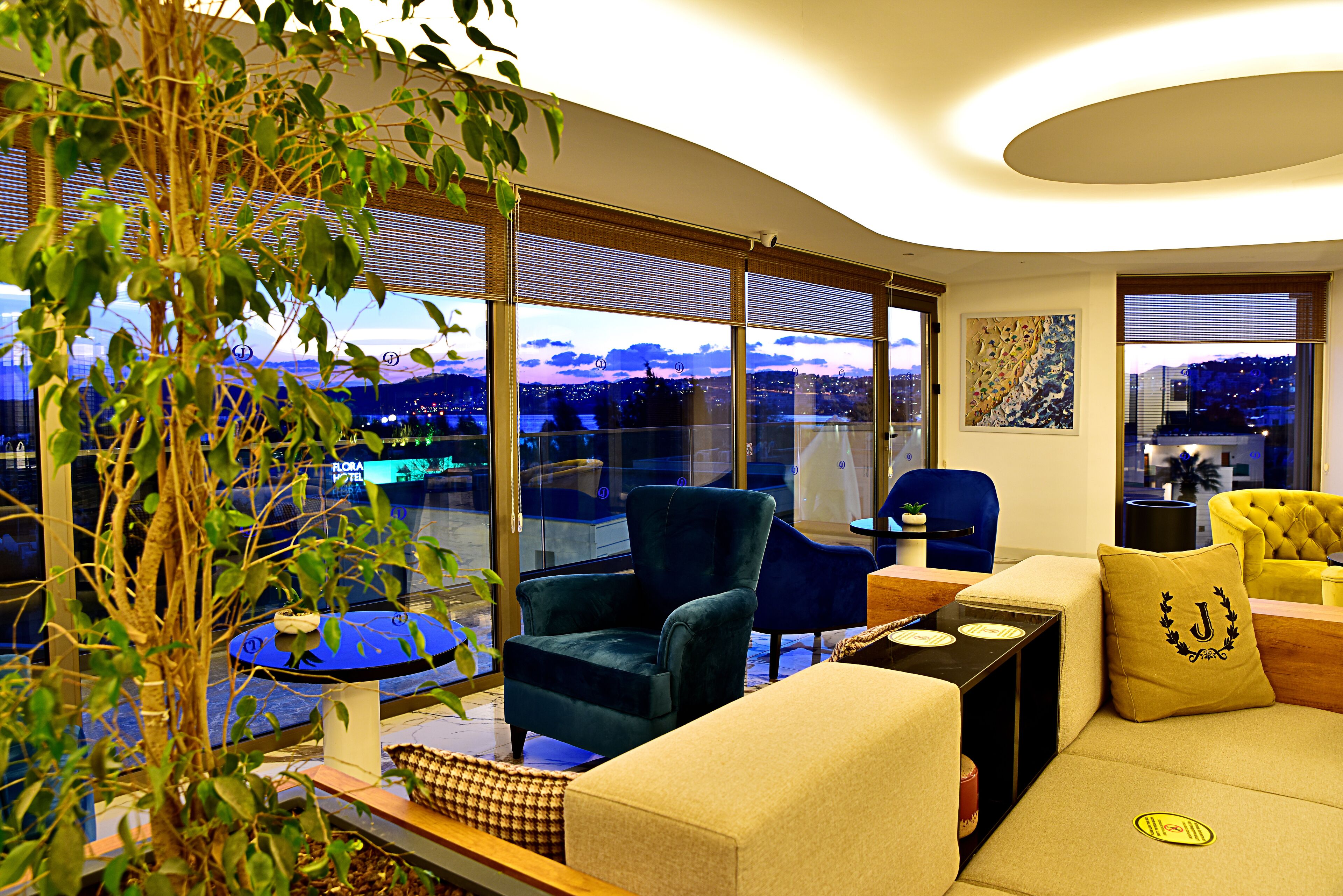 Un salon moderne avec une grande fenêtre, un fauteuil bleu, un canapé beige et un autre fauteuil jaune.